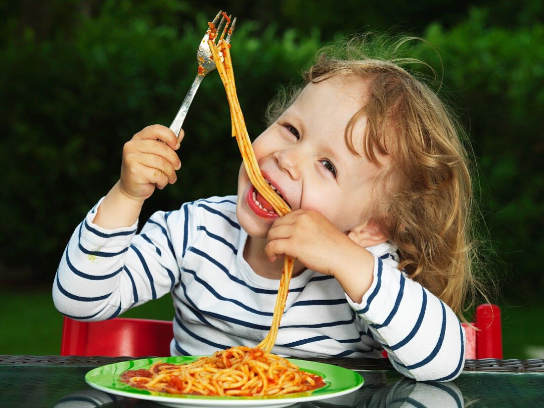 Girl eating spaghetti with tomato sauce