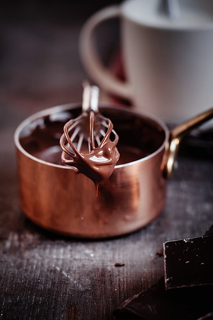 Geschmolzene Schokolade tropft von einem Schneebesen auf einem Kupfertöpfchen