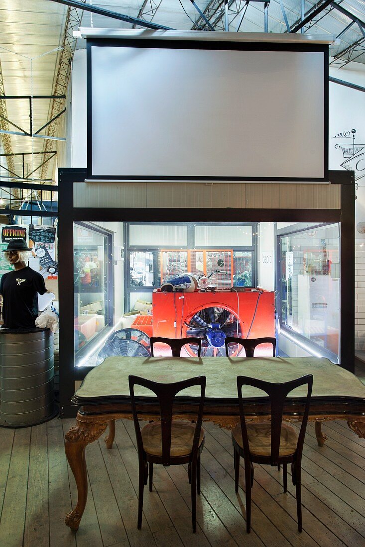 Ornate dining table with gilt legs in front of large ventilation fan and projector screen