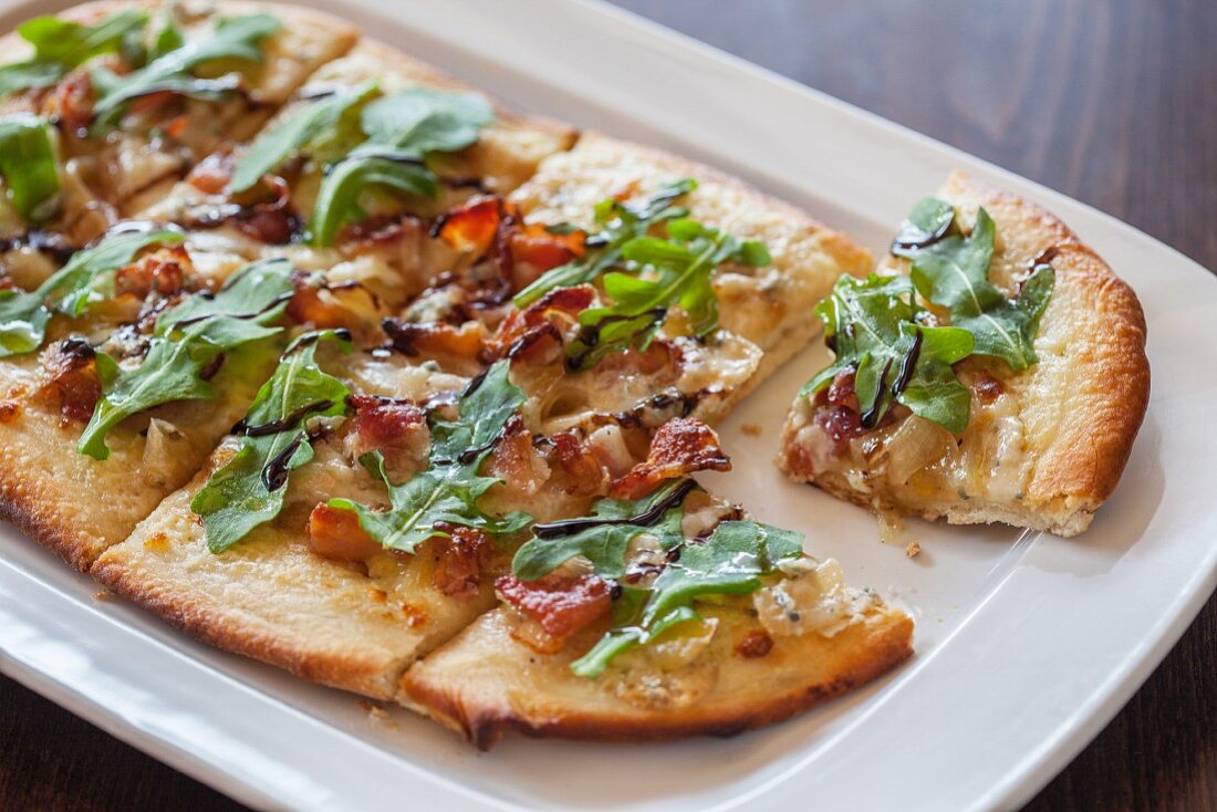 A pizza topped with bacon, gorgonzola and rocket