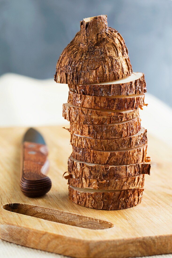 Cassavva roots, sliced, on a chopping board with a knife