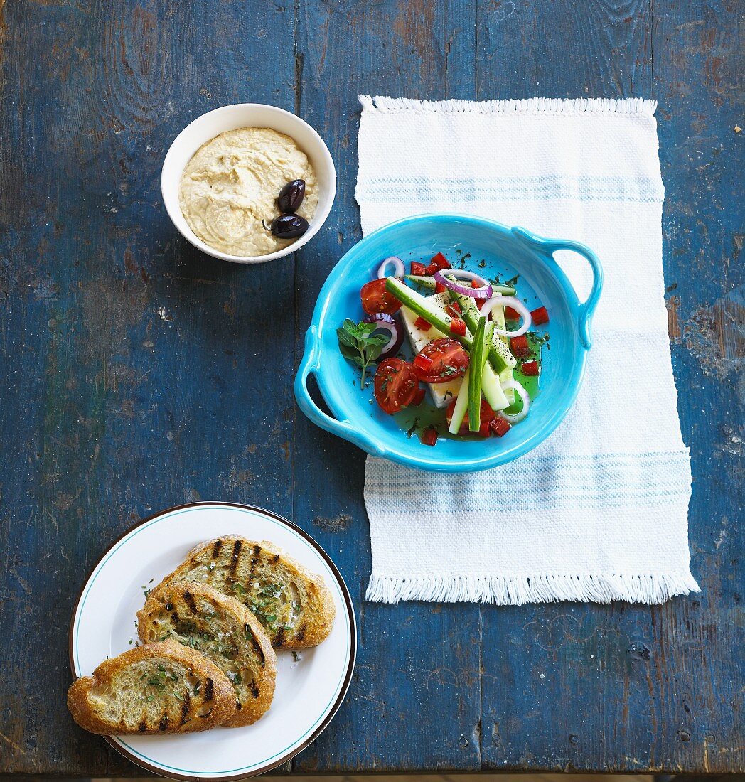 A Greek salad with a dip and a toasted bread