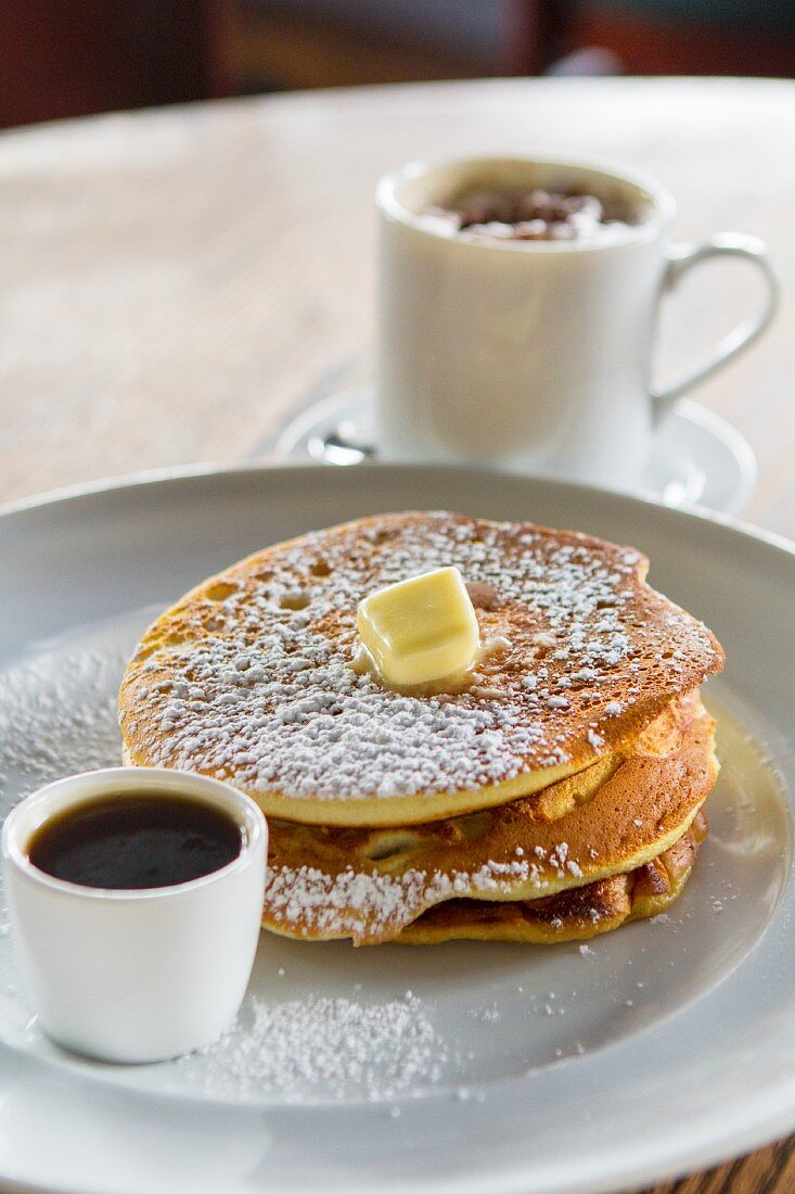A stack of pancakes with sugar, butter and coffee
