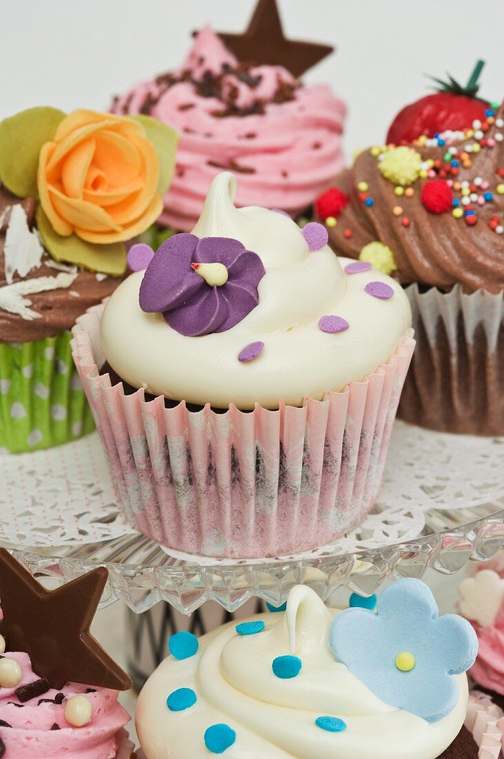 Verschiedene Cupcakes mit Zuckerblumen, Schokosternen und Zuckerperlen