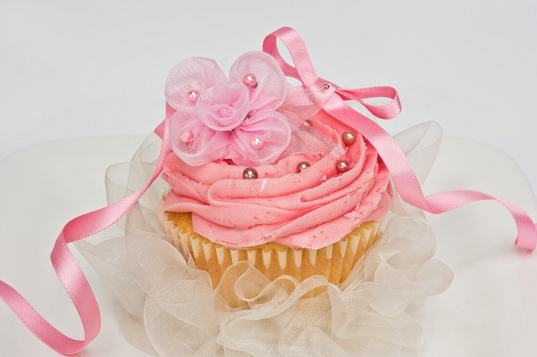 A pink cupcake with chiffon flowers and a bow