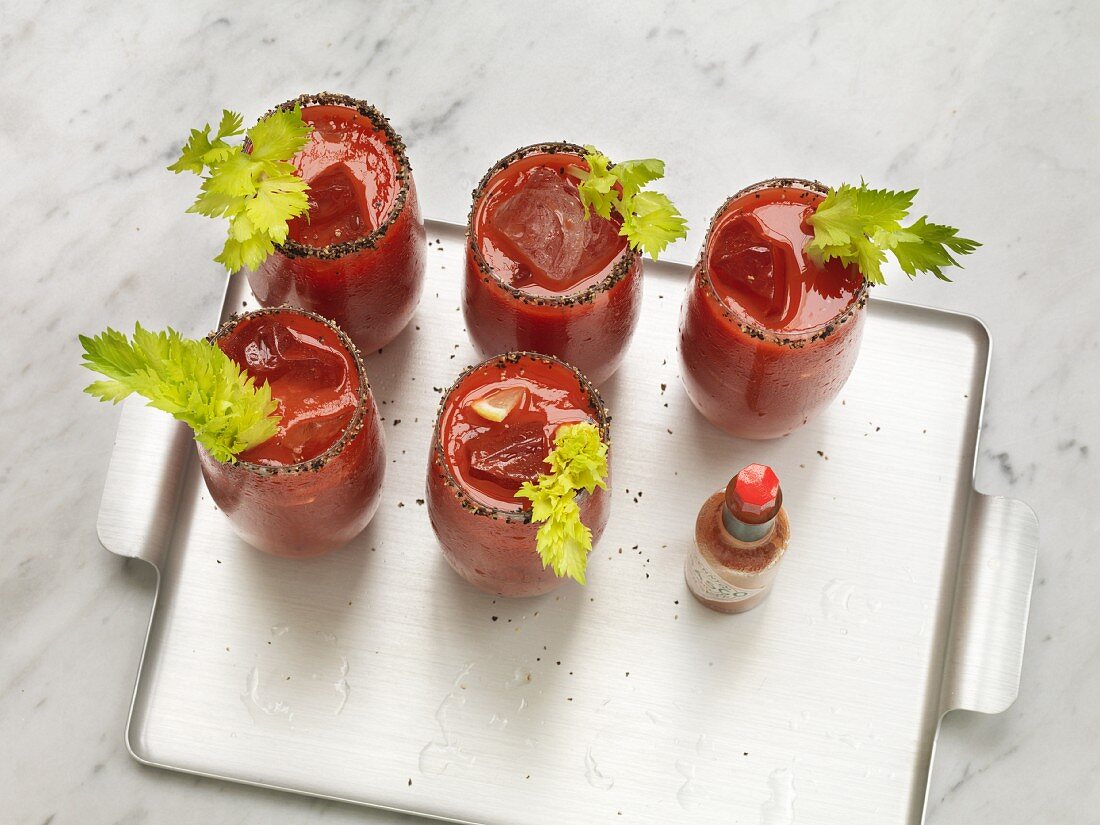Five Bloody Marys garnished with celery on a tray