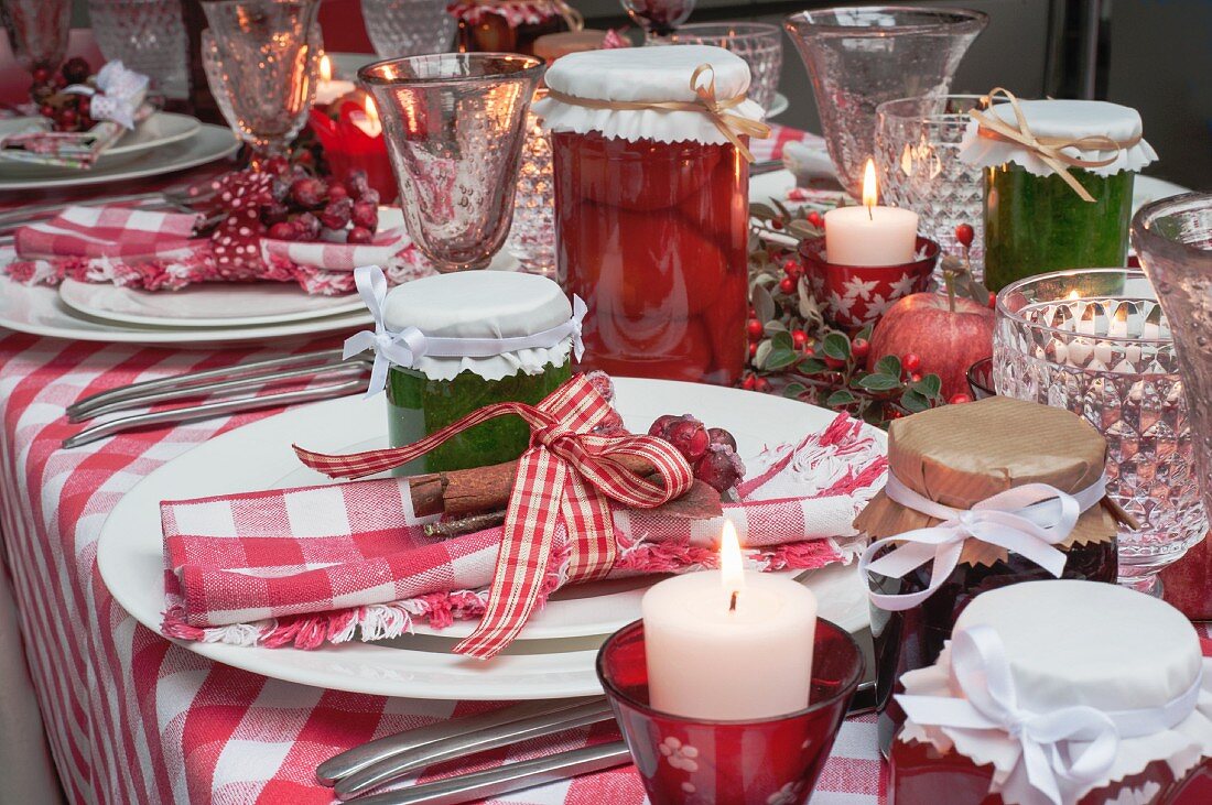 A Christmas table laid with a red checked tablecloth, napkins, jars of jam and candles