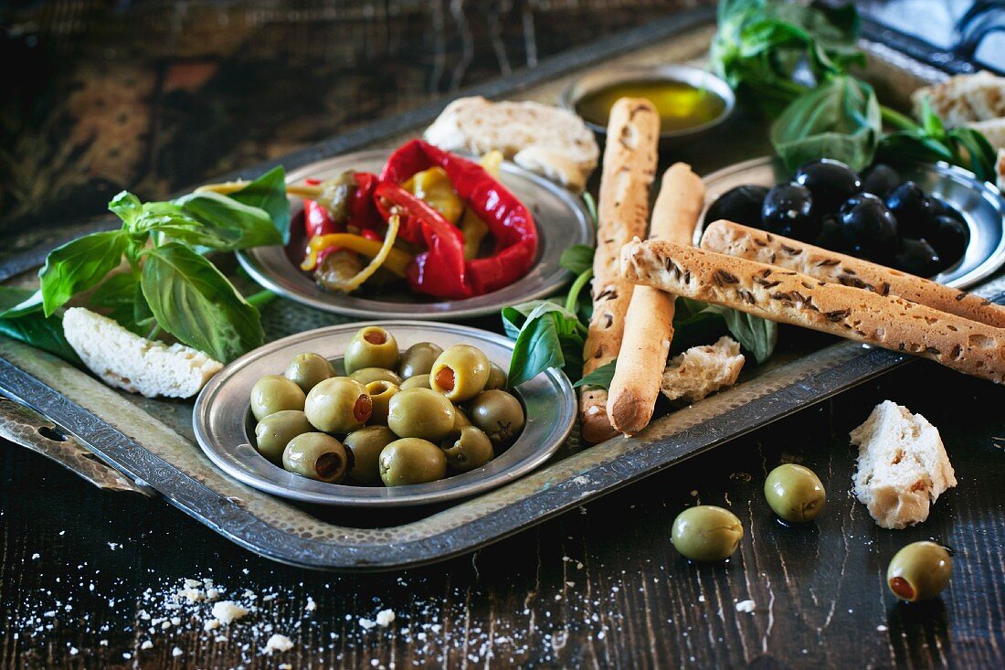 Gemischte Antipasti, Oliven und Paprika mit Brotsticks und Basilikum auf Tablett