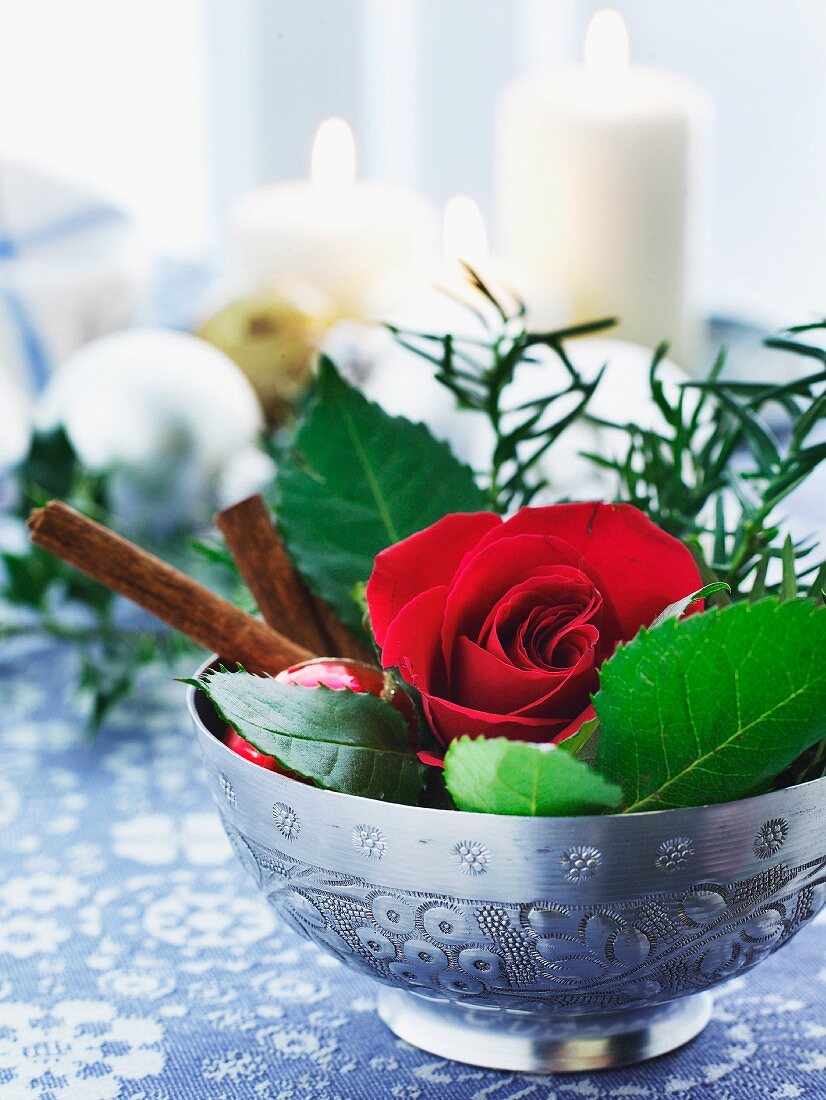 A Christmas table decoration with a rose and cinnamon sticks in a bowl