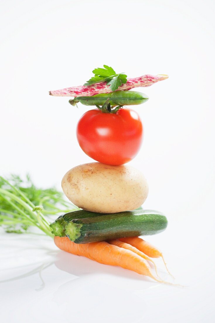 A stack of vegetables consisting of carrots, courgettes, a potato, a tomato, a pea pod and a borlotti bean