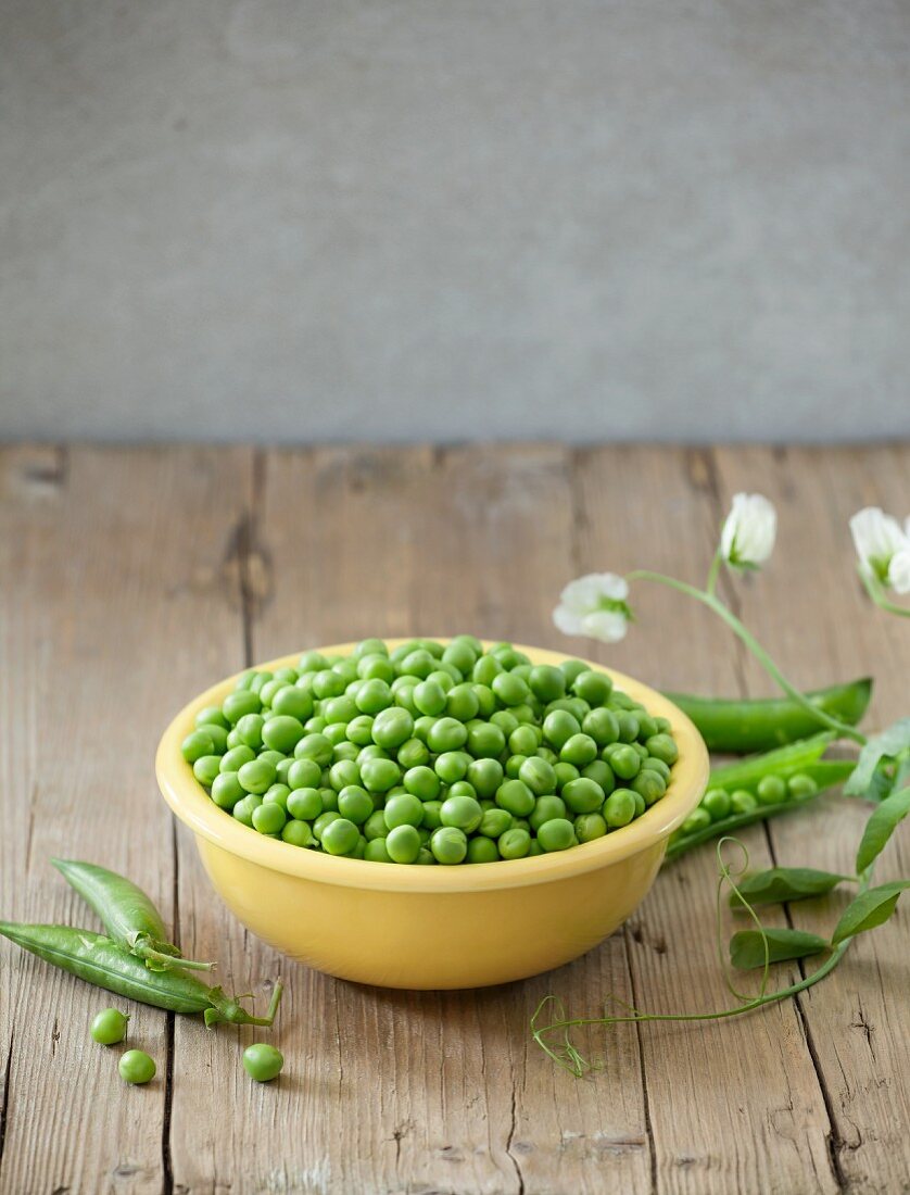 A bowl of fresh peas on a wooden surface
