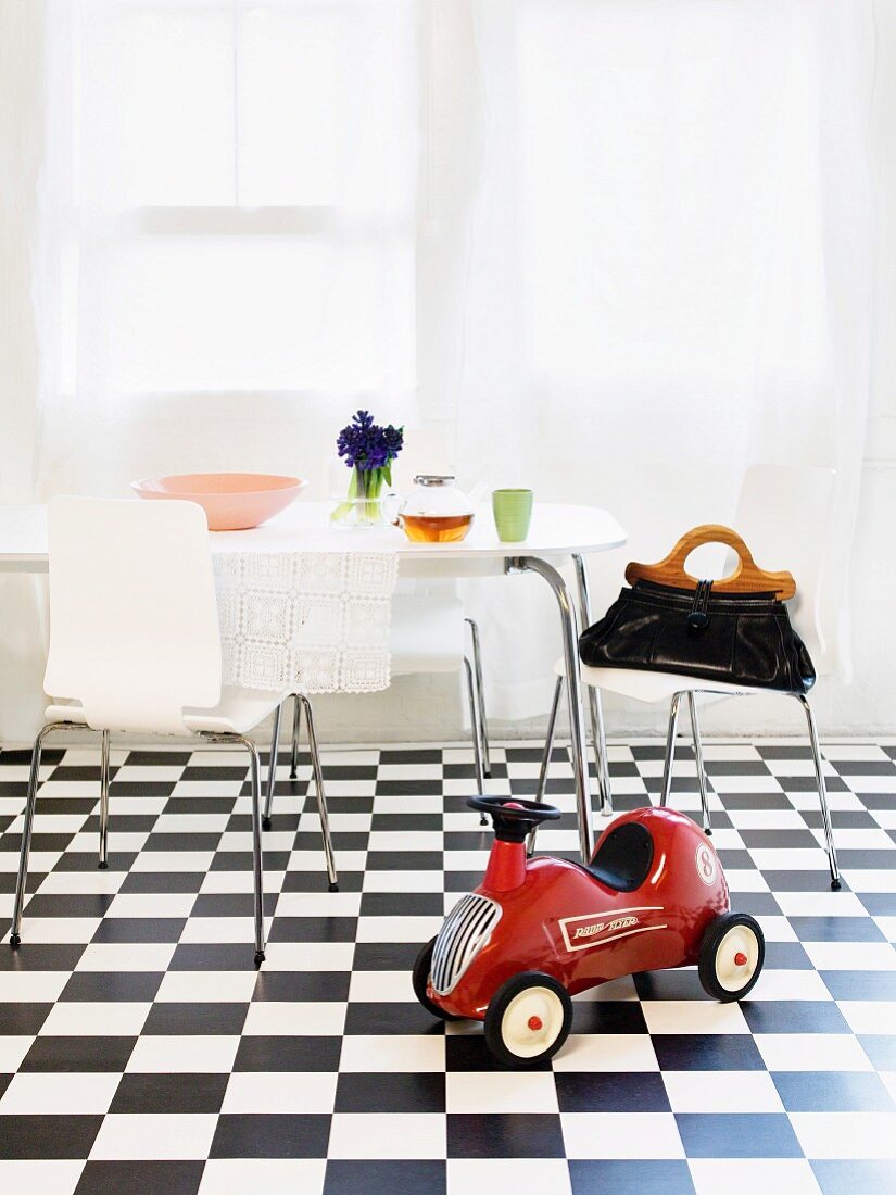 A red children's car with an eating area in the background on a black and white checked floor