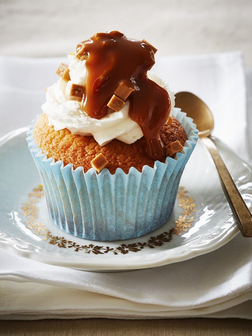 A cupcake topped with cream cheese frosting and caramel sauce