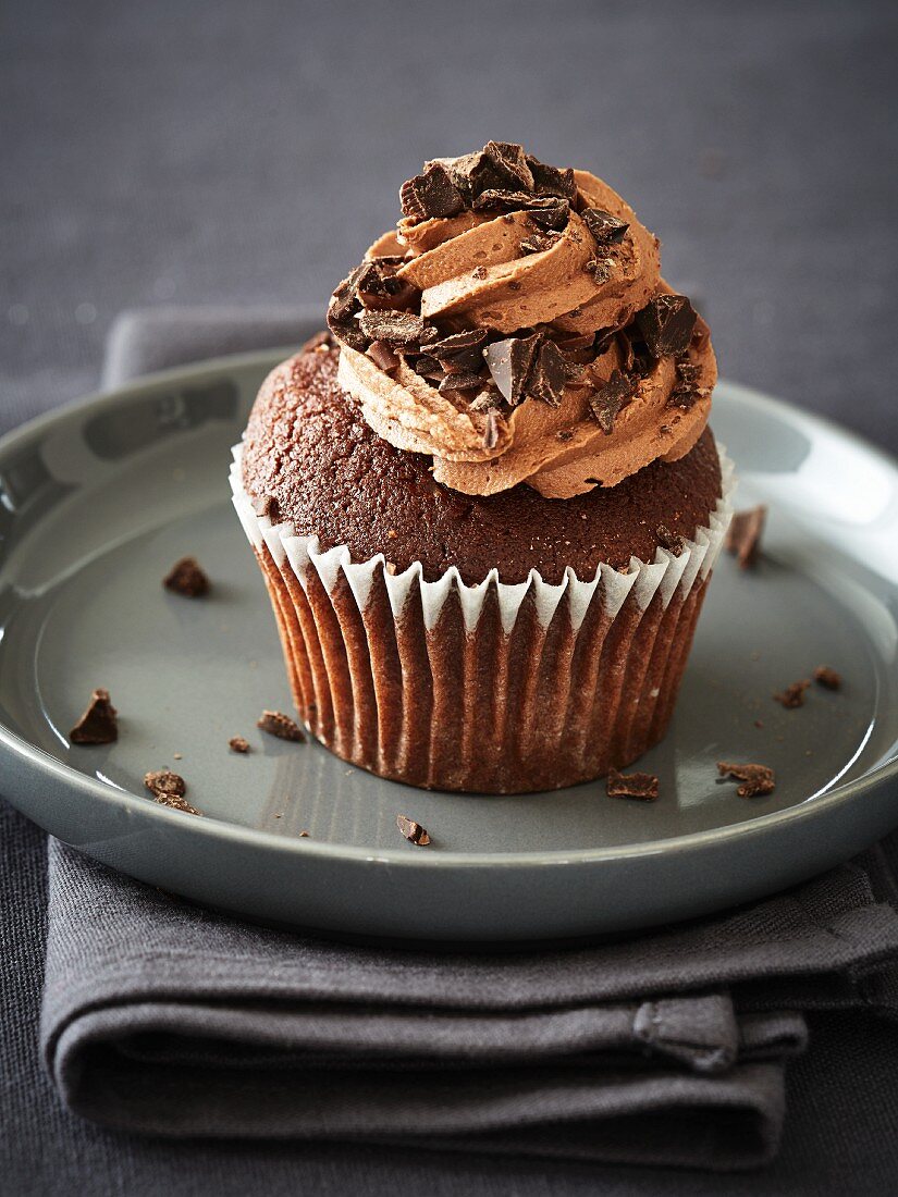 A chocolate cupcake with buttercream and pieces of choc