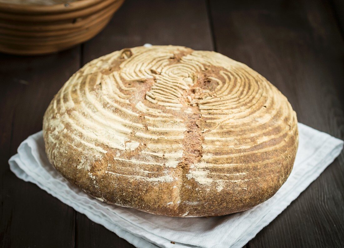 A freshly baked homemade loaf of wheat sourdough bread on a wooden table