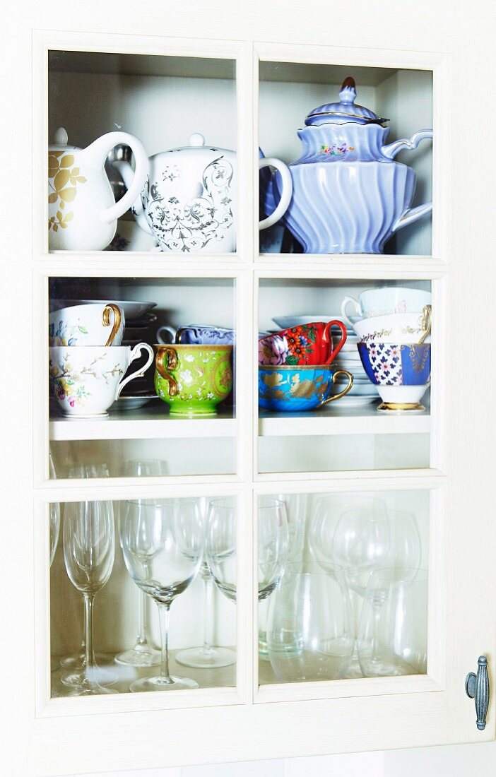 Teapots, cups and glasses in crockery cupboard with lattice door