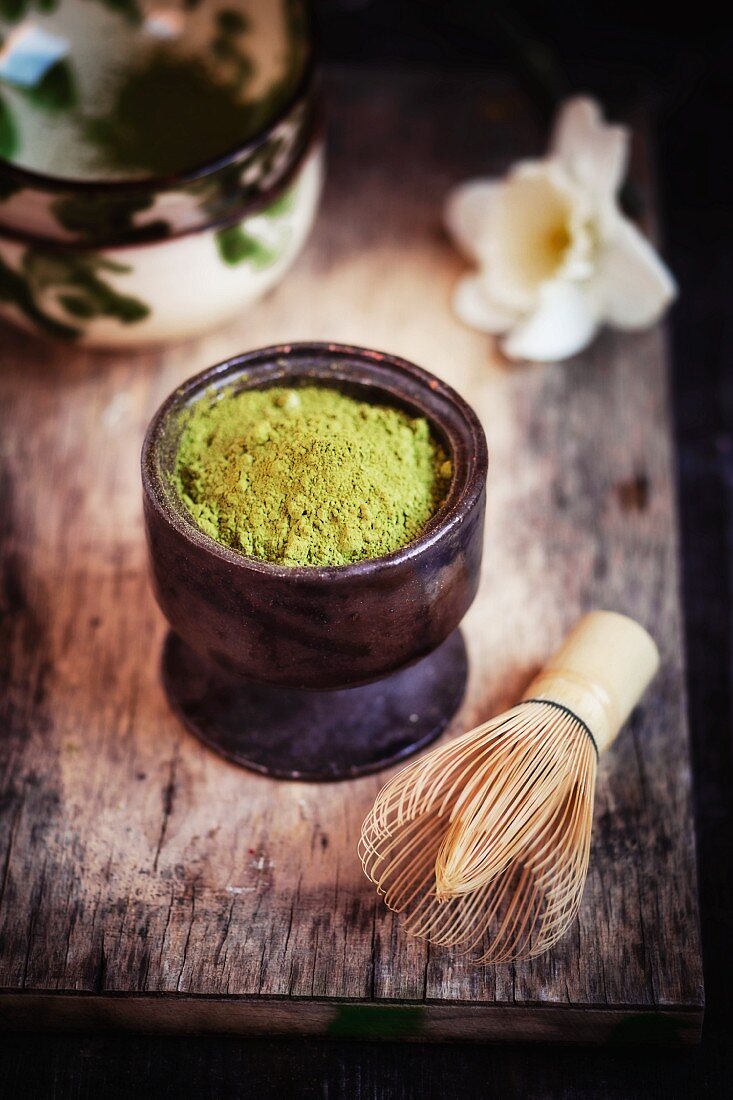 Matcha tea powder in a ceramic pot with tea bowls and a bamboo whisk