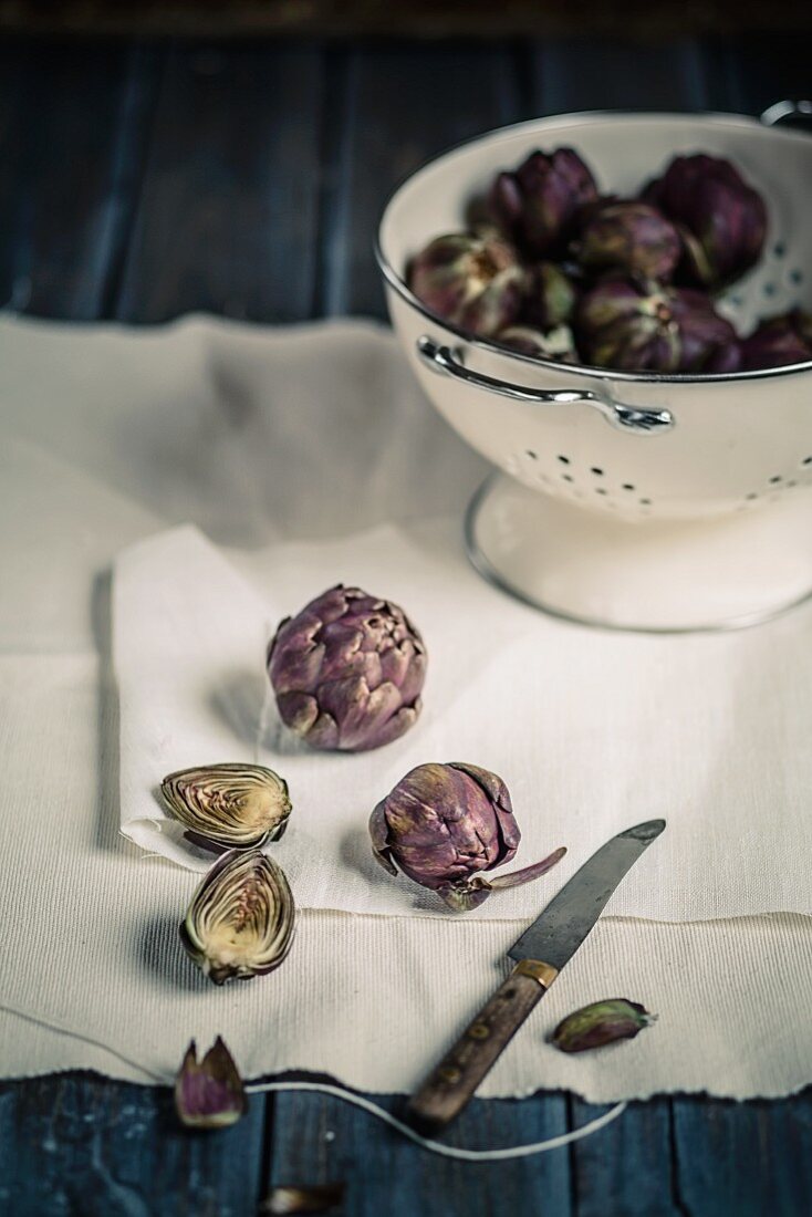 Artichokes, whole and halved, in a colander and on a cloth