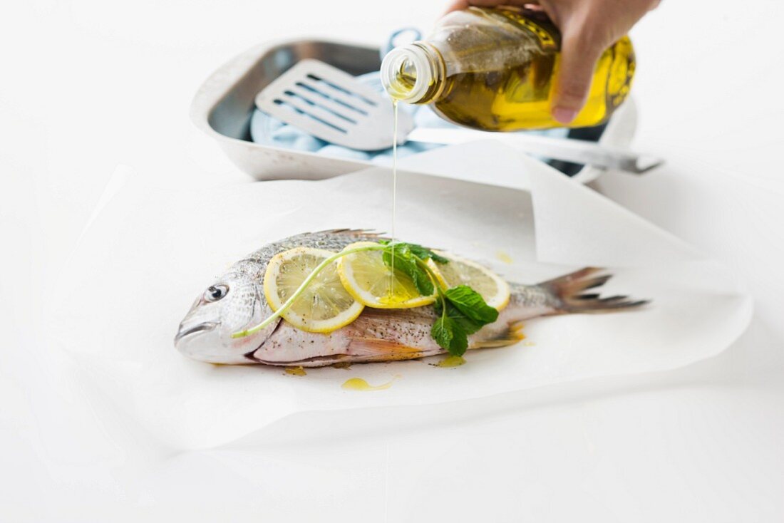 Olive oil being drizzled over seabream with lemon and basil