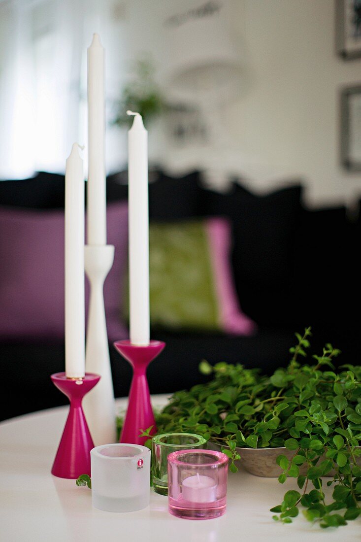 Set of pink and white candlesticks and tealight holders next to bowl of leafy twigs