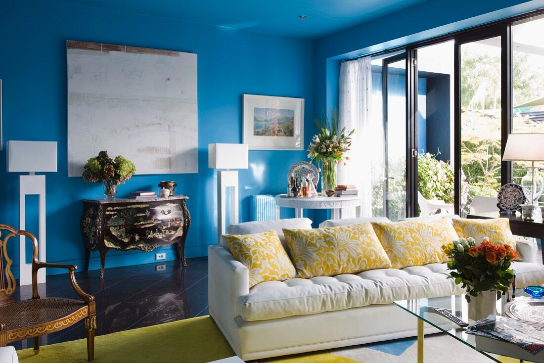 White sofa next to glass terrace doors in front of Rococo chest of drawers against blue wall in living room