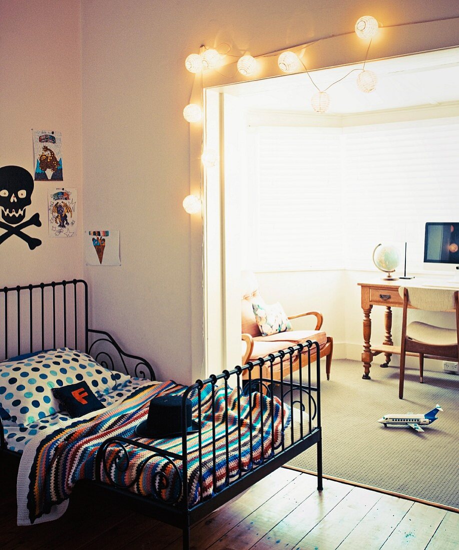 Retro metal bed in teenager's room, wide open doorway decorated with lanterns and view into traditional lounge area