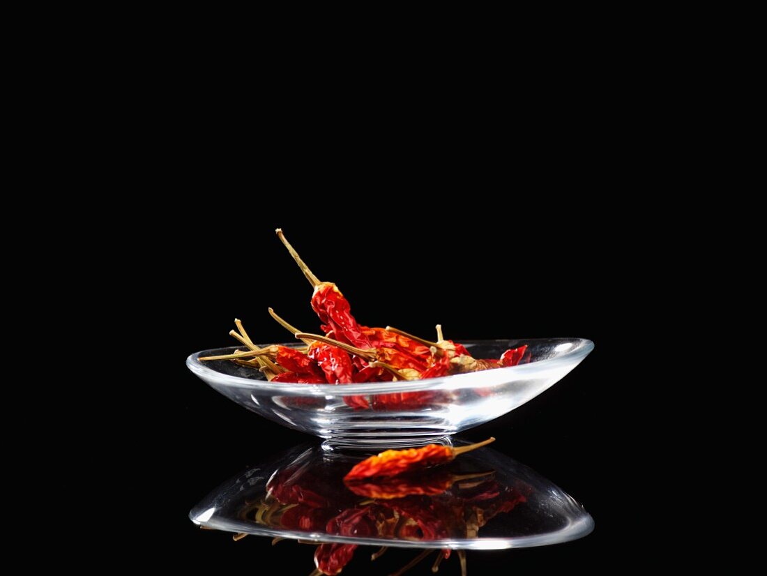 Dried chilli peppers in a glass dish against a black background
