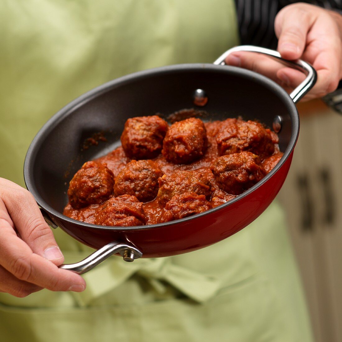 A man holding a pan of meat balls in tomato sauce