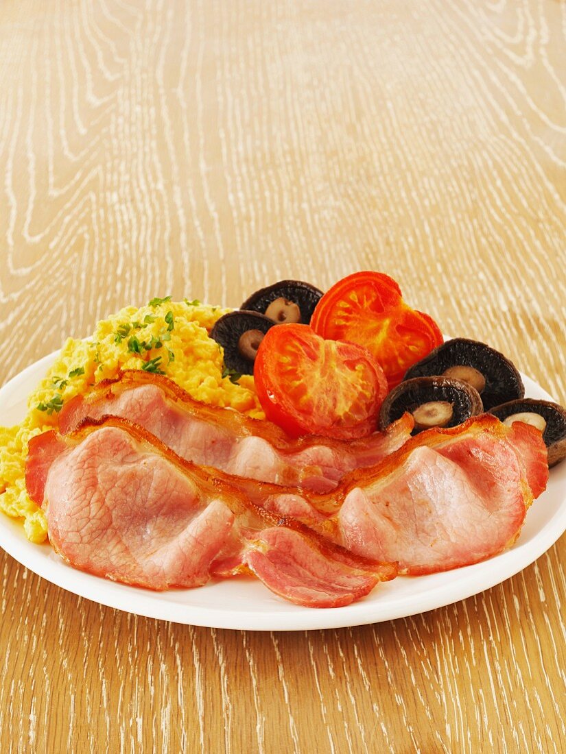 Frühstücksteller mit Bacon, Rührei, Pilzen und Tomaten
