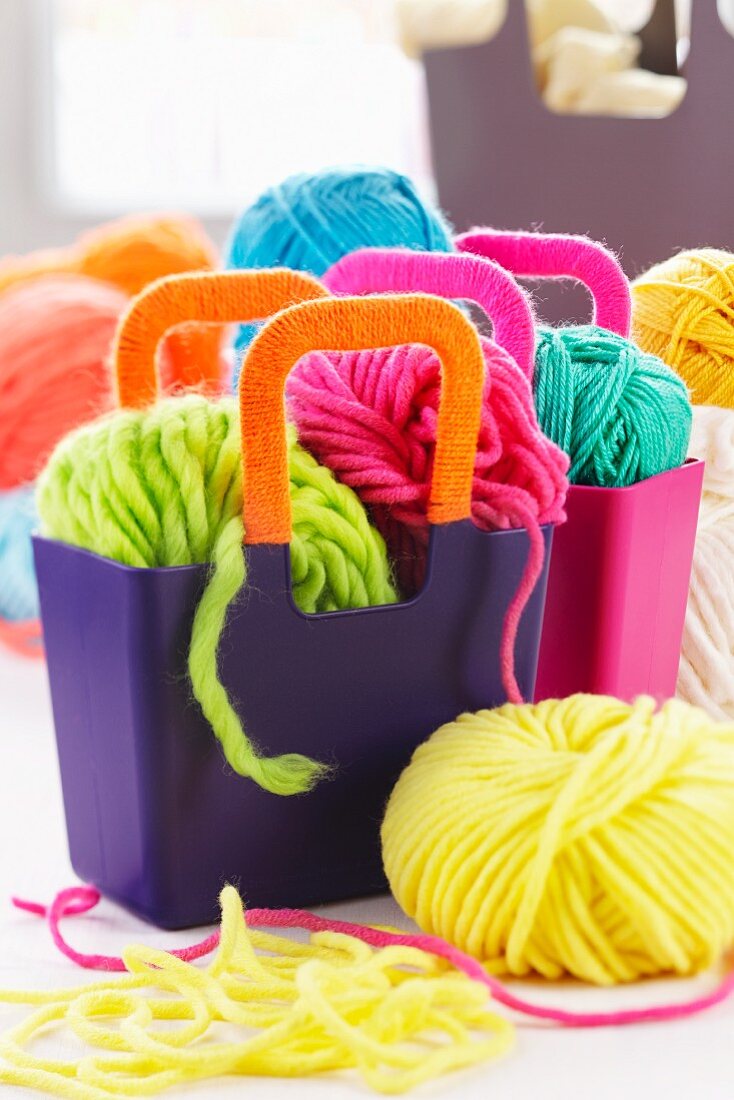 Balls of brightly coloured wool in purple plastic bags with wool-wrapped handles