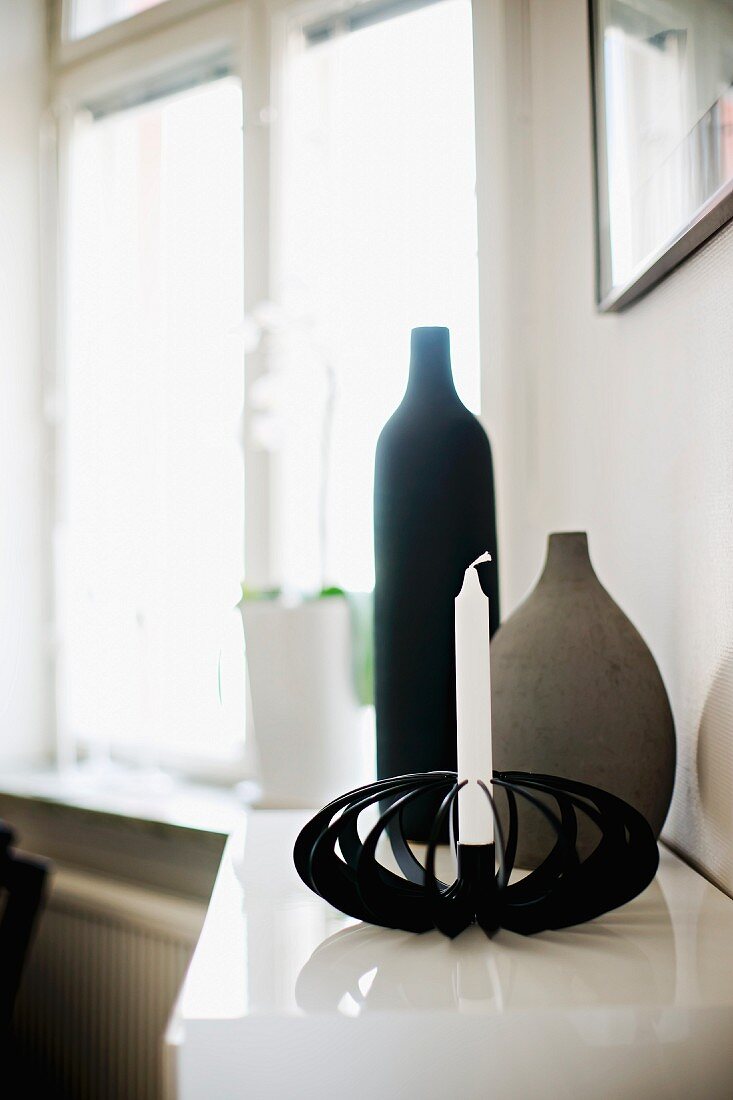 Still-life arrangement of candlestick made from black metal slats and hand-crafted ceramic vessels