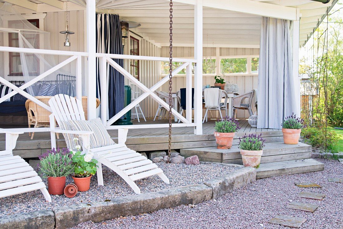 White wooden loungers on gravel terrace in front of veranda of wooden house