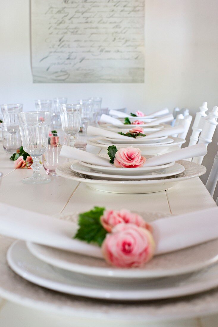 White place settings with roses and linen napkins on white wooden table