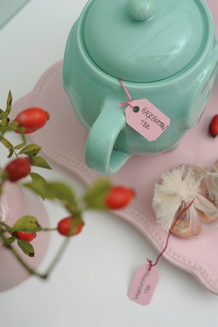 Turquoise teapot of rose hip tea and sprig of rose hips in vintage ambiance
