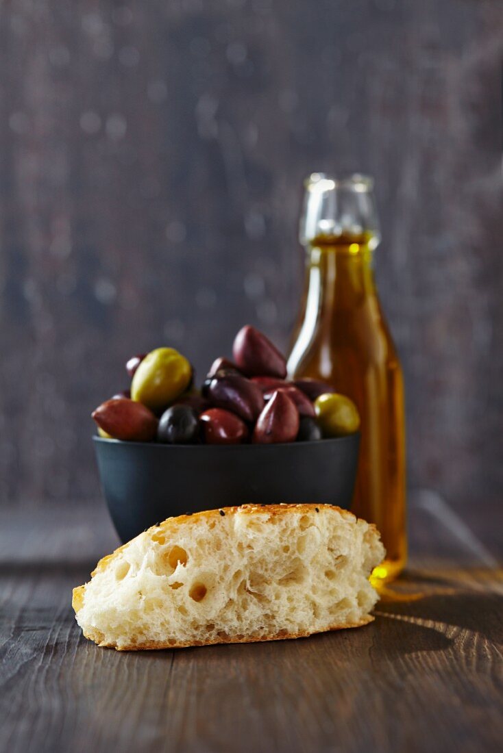 A slice of unleavened bread, olives and a bottle of olive oil