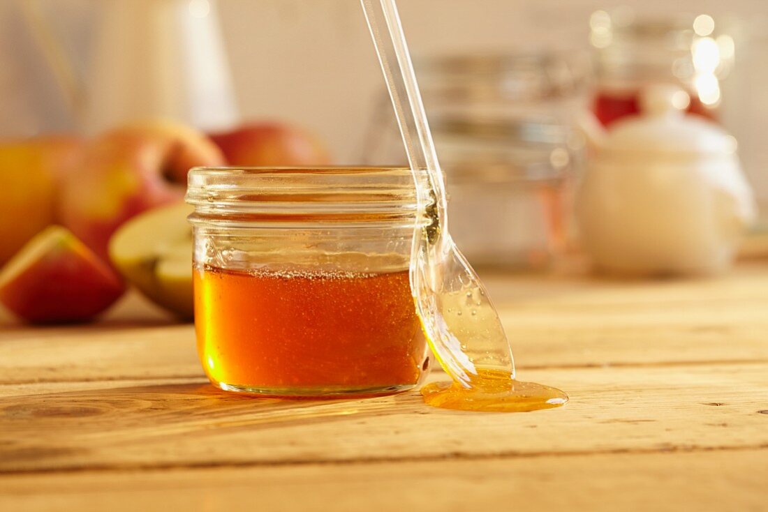 A jar of honey with a spoon with fresh apples in the background
