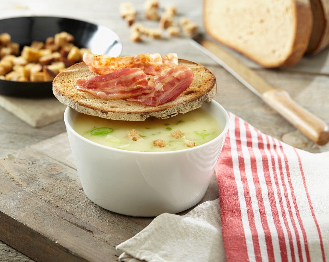 Potato soup with croutons and a slice of bread topped with bacon