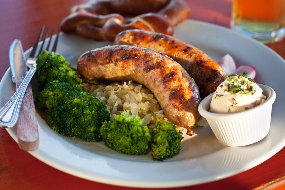 Two sausages served with broccoli, sauerkraut, Obazter (Bavarian cream cheese) and a pretzel