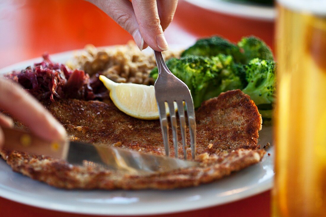 Escalope á la viennoise being sliced. Served with broccoli and red cabbage