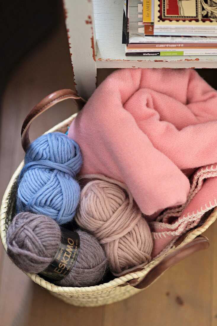 Balls of wool in various colours and pink blanket in basket on floor