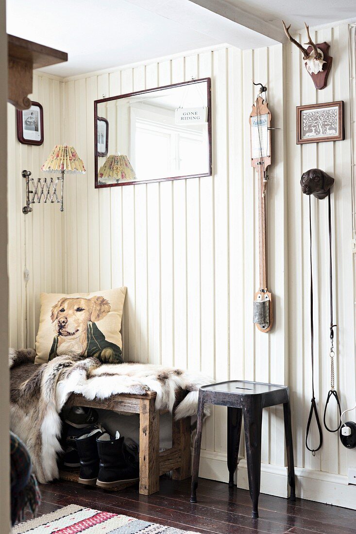 Classic metal stool next to bench with animal-skin blanket and cushions against white wooden wall in foyer