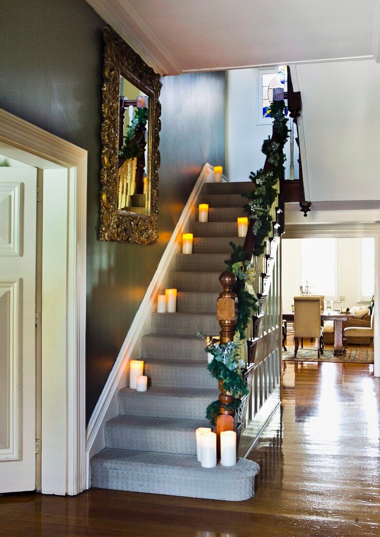 Brennende Kerzen auf Treppenstufen in traditionellem elegantem Villenflur, Blick durch raumhohen Durchgang ins Wohnzimmer