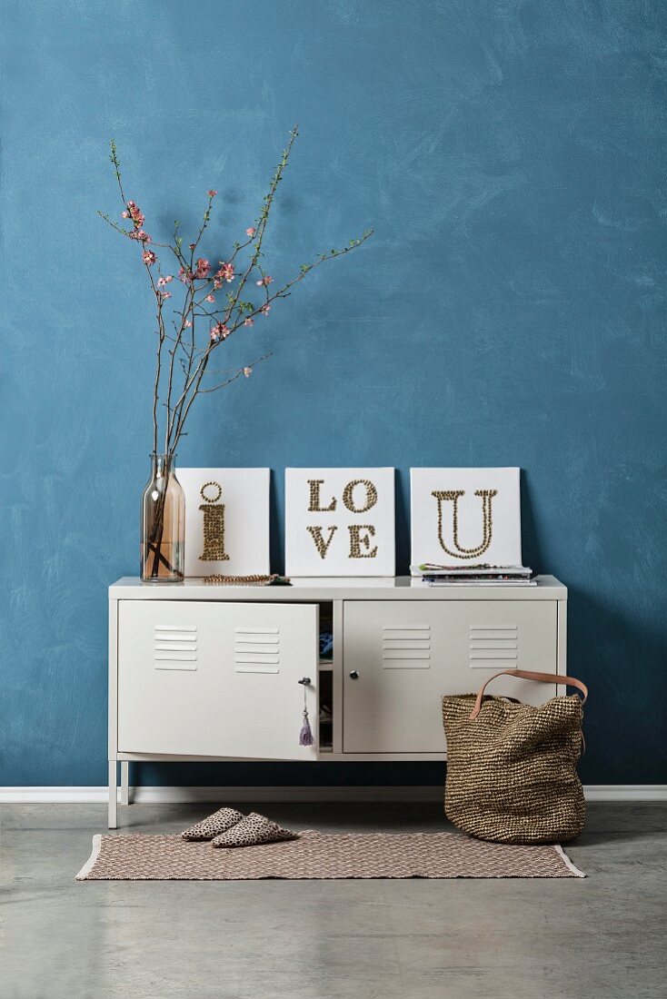 Vintage arrangement of white locker against blue-grey wall and three DIY string art pictures