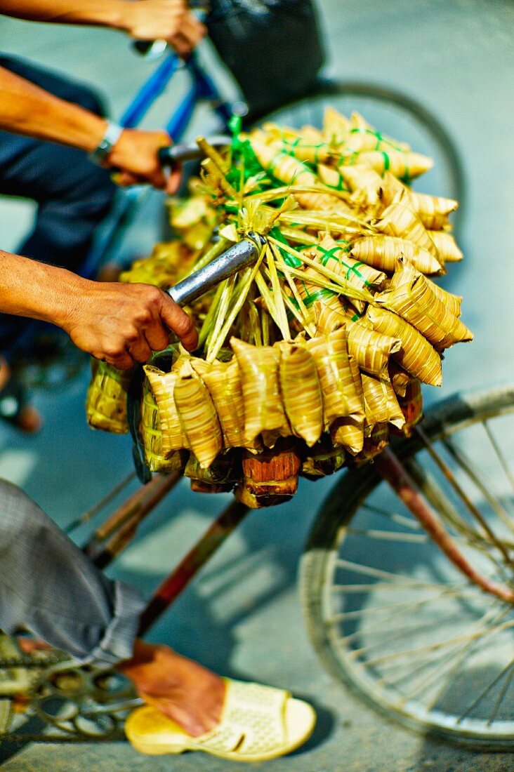 Verkäufer fährt mit Bündeln von Bananenblattpäckchen auf dem Fahrrad zu einem Markt in Saigon (Vietnam)