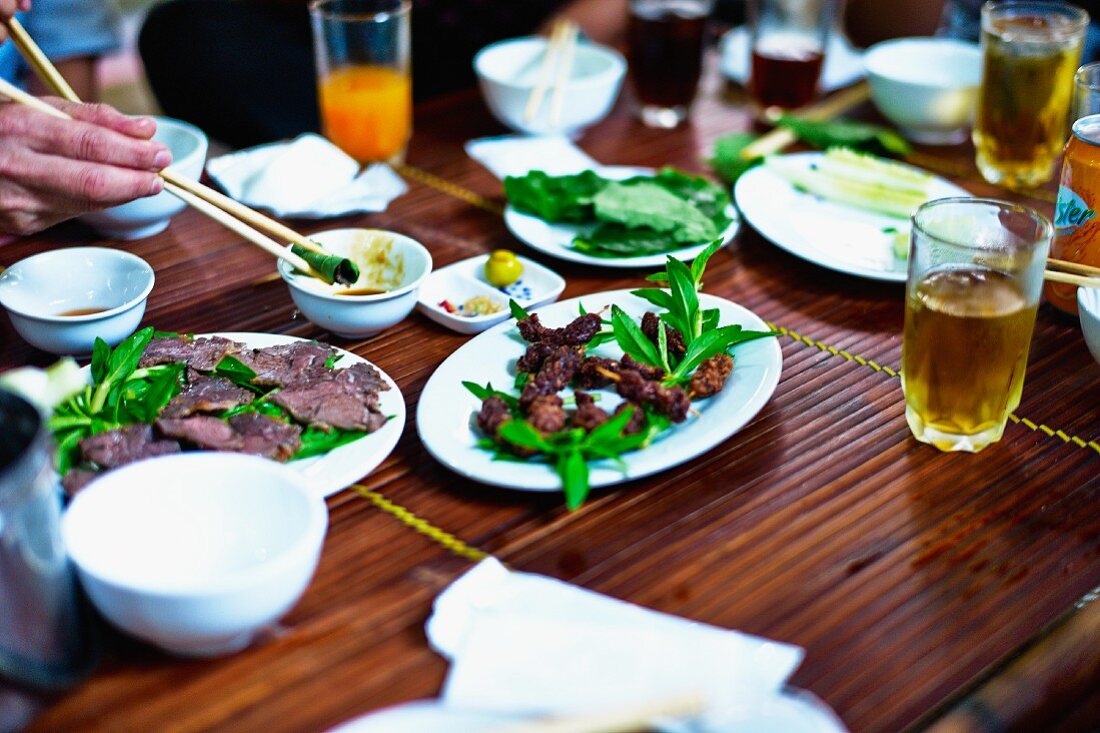 A hand holding a piece of fried water buffalo in chopsticks and dipping it in sauce, Vietnam