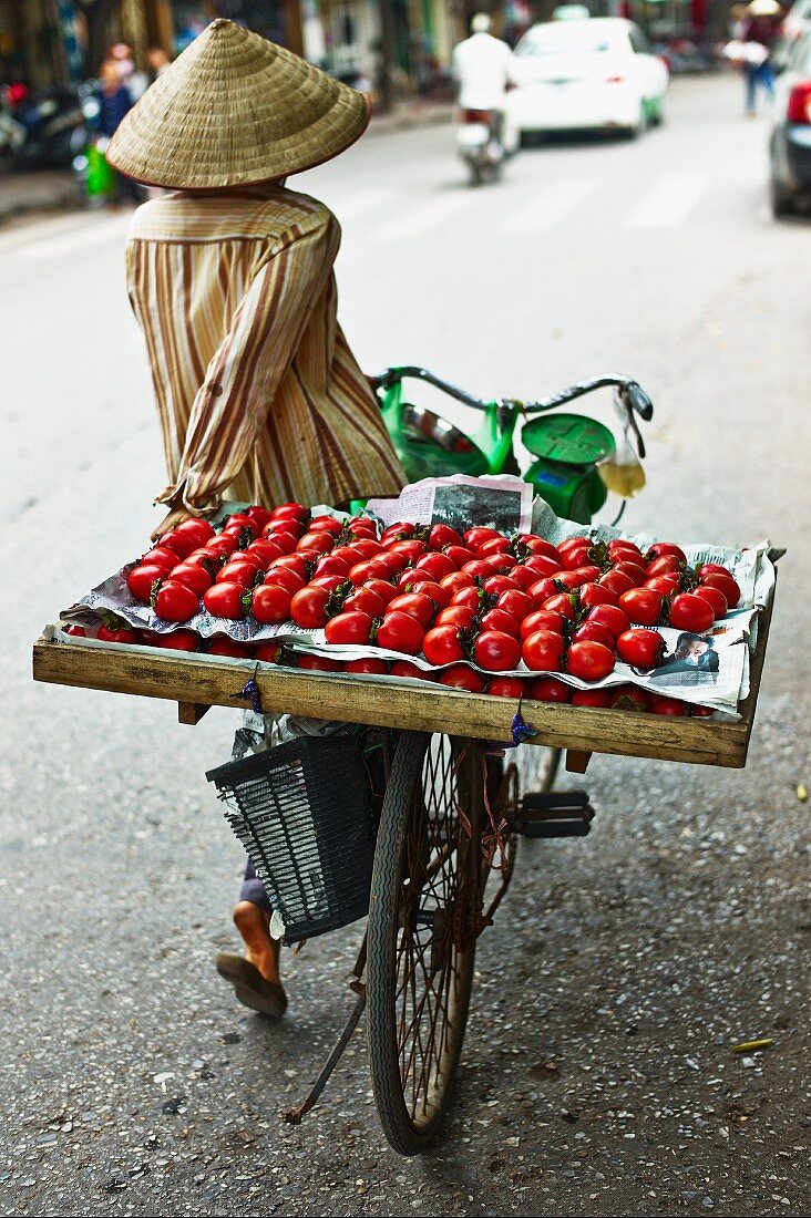 A Vietnamese person transporting a crate of tomatoes on a bicycle