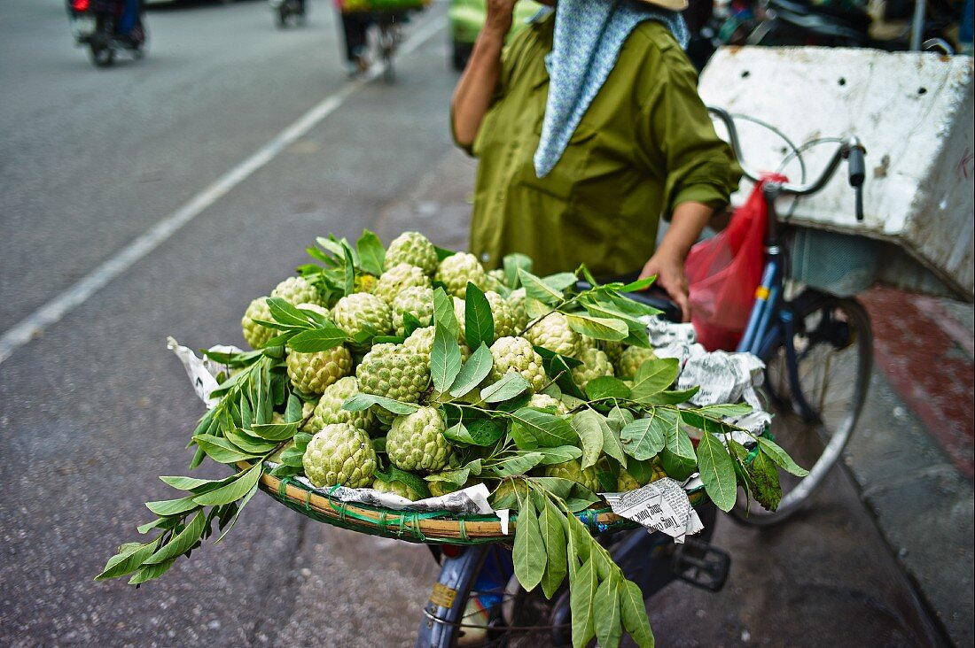 A Vietnamese woman transporting a basket of sugar apples on a bicycle