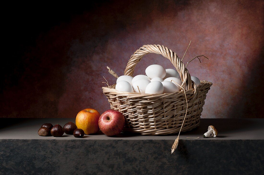 Fresh eggs in a wicker basket with apples, chestnuts and mushrooms