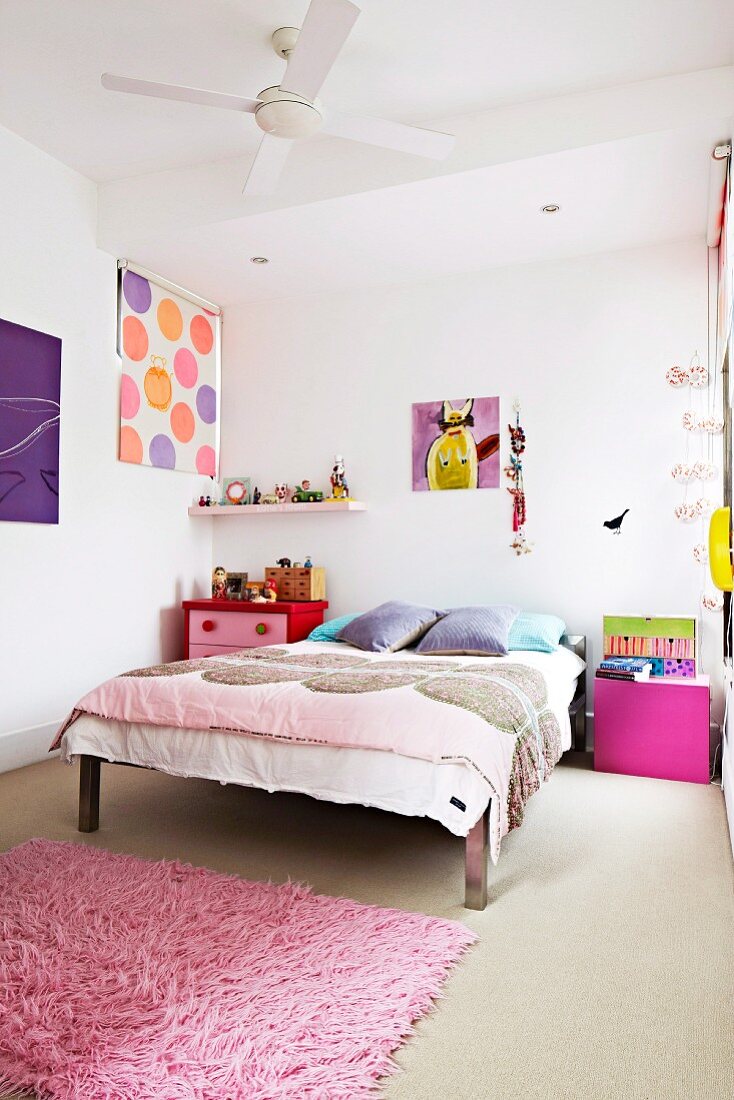 Bed with bedspread, pink bedside cabinet and pink flokati rug in cheerful child's bedroom