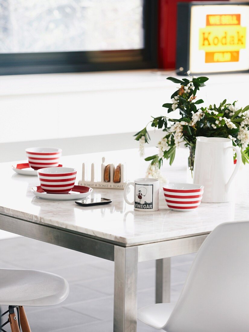 Red and white striped cups on dining table with marble top and metal frames combined with Eames shell chairs